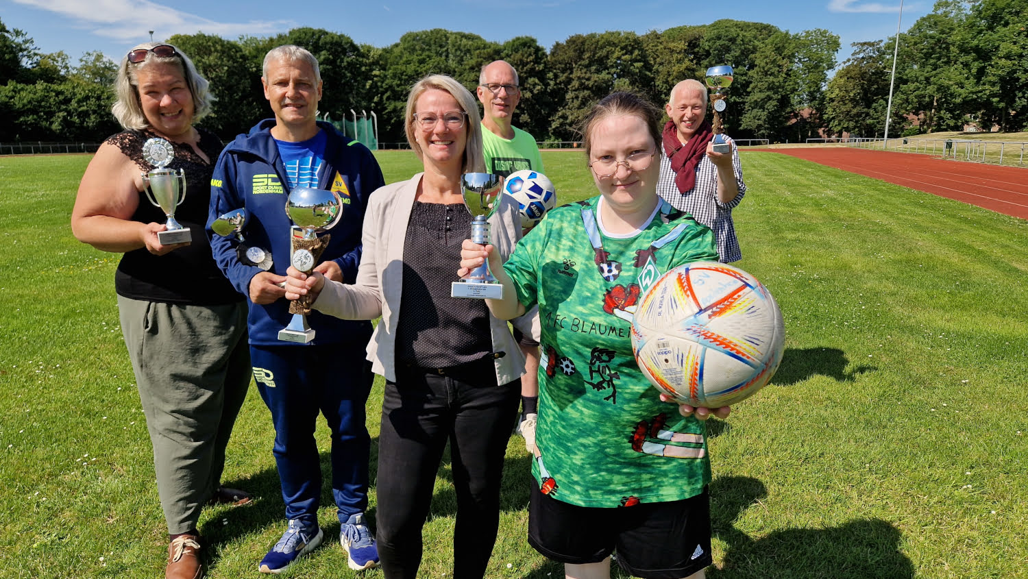 Beteiligte des inklusiven Fußballturniers mit Pokalen und Fußball